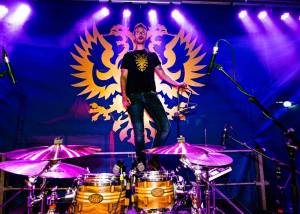 Mann steht auf einem Hocker vor einem Schlagzeug