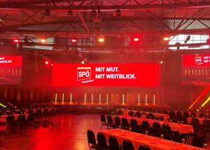 Halle mit aufgebauten Tischen und rotem Bühnenbild